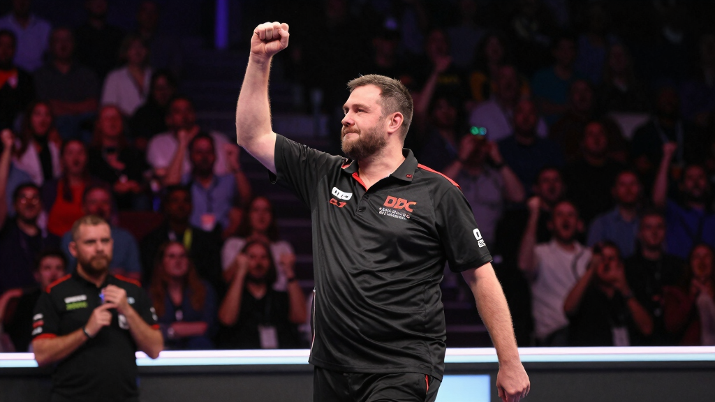 Professional darts player celebrating championship win on stage, crowd roaring, spotlights